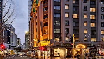 Ett hotell med flera våningar, en framträdande entré, ett område för fotgängare och en utsikt över gatan med trafikljus.