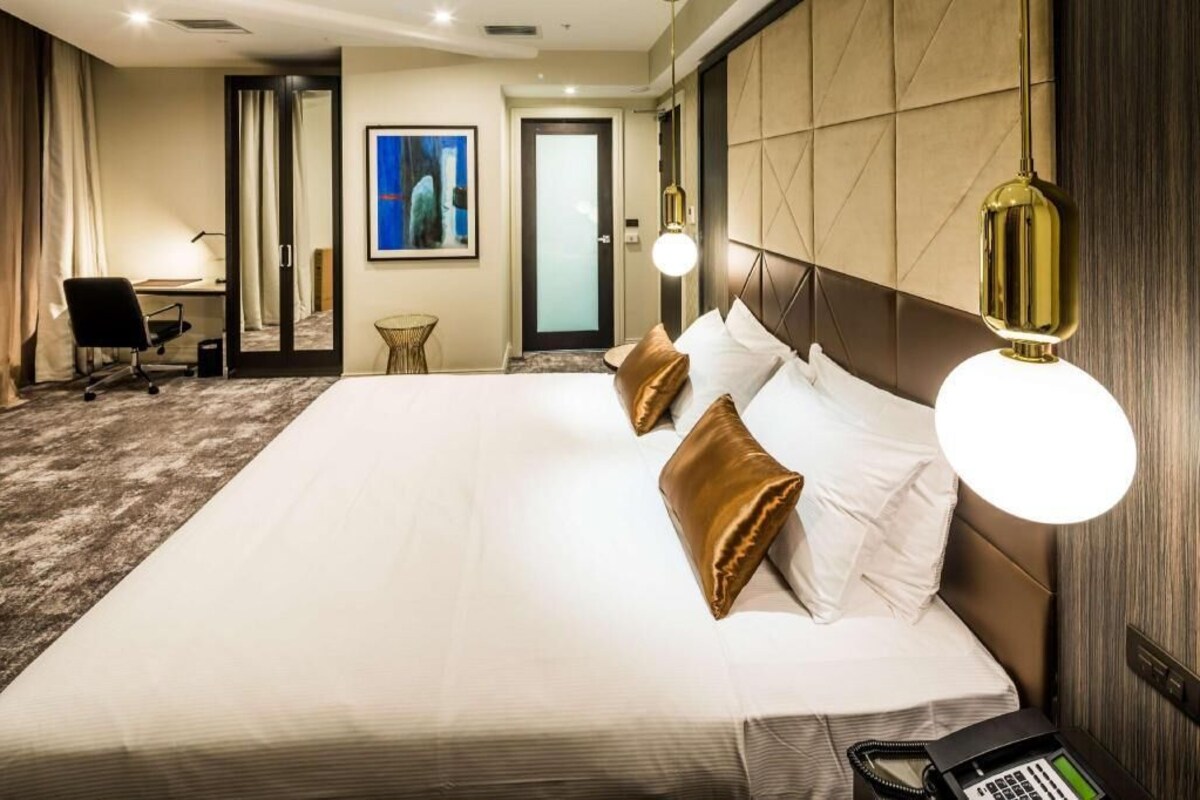 A hotel room with a large bed, a desk, a chair, a phone, and a door.