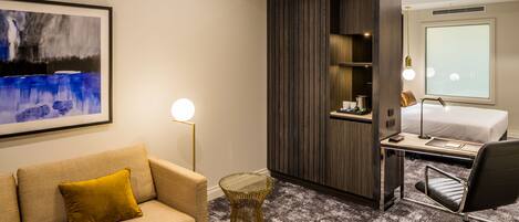 A hotel room with a sofa, a desk, a chair, a bed, and a large window.