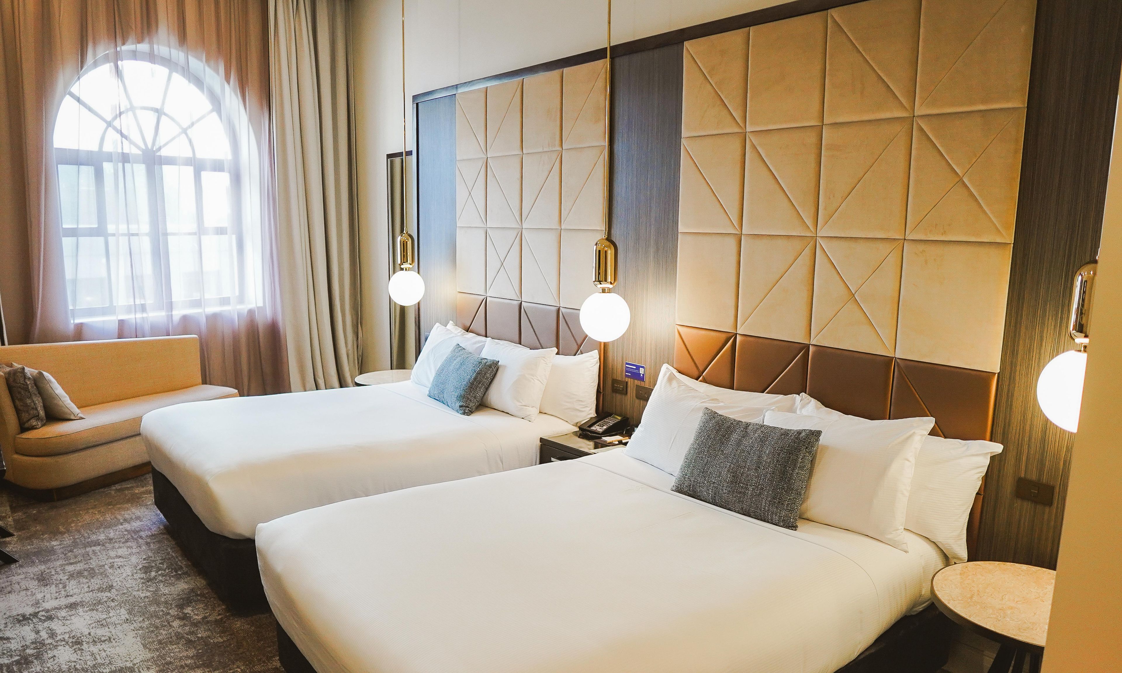 A hotel room with two beds, a sofa, and a large window.