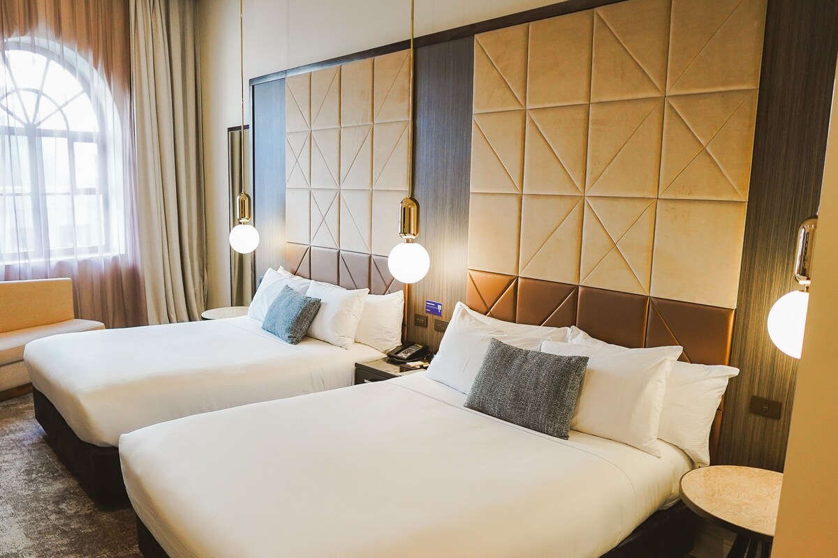 Habitación de hotel con dos camas, un sofá y un ventanal grande.