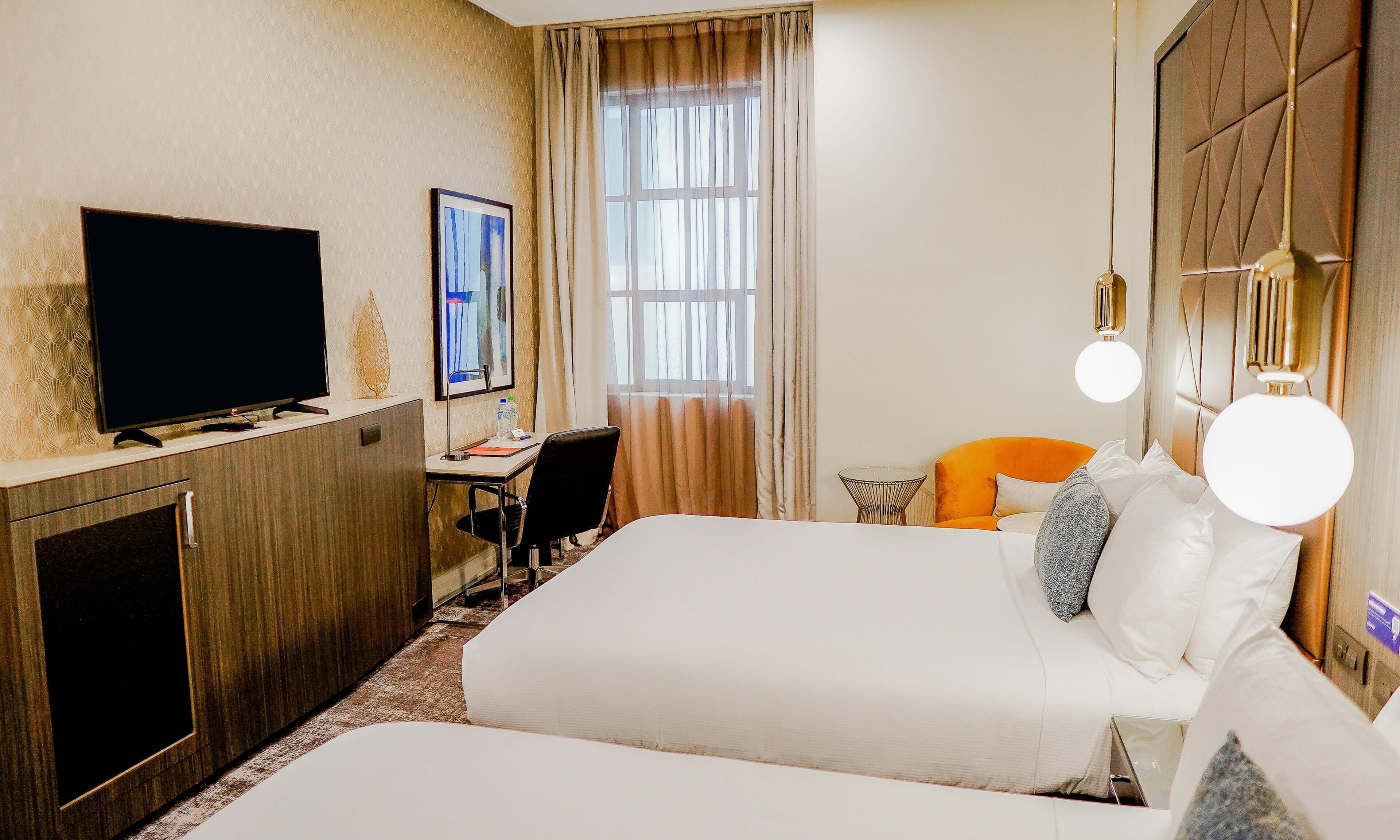 A hotel room with a bed, a desk, a television, and a window with curtains.