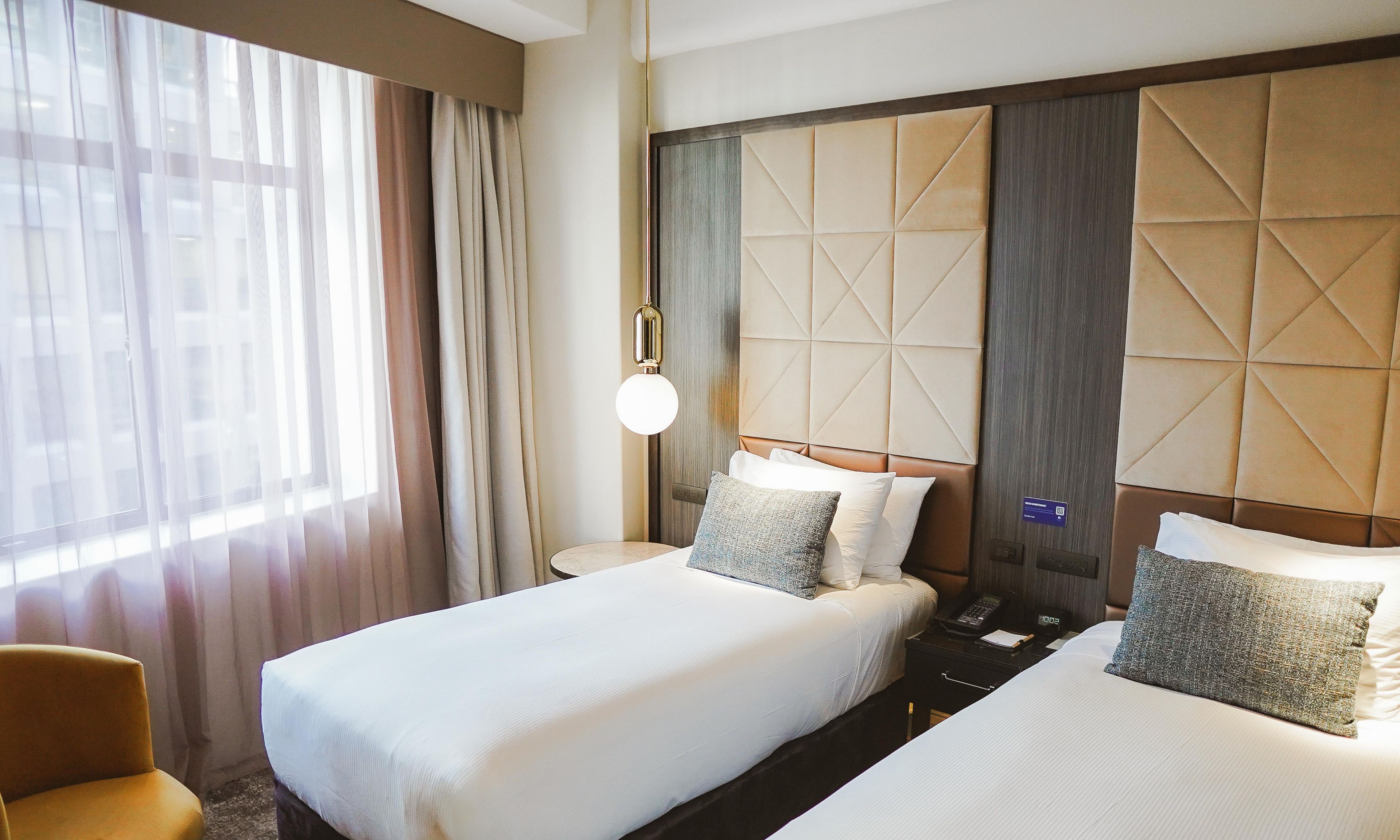 Habitación de hotel con dos camas, una mesita de noche, un teléfono y una ventana con cortinas.