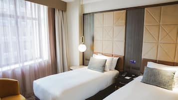 Habitación de hotel con dos camas, una mesita de noche, un teléfono y una ventana con cortinas.