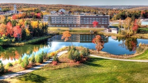 A multi-story building with a flat roof, surrounded by a lake and autumn foliage. - Radisson Hotel Kingswood Hotel Fredericton, NB (Hanwell)