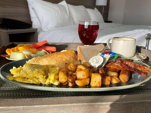 A breakfast plate with eggs, toast, bacon, potatoes, and fruit on a table with a bed and a nightstand in the background. - Radisson Hotel Kingswood Hotel Fredericton, NB (Hanwell)