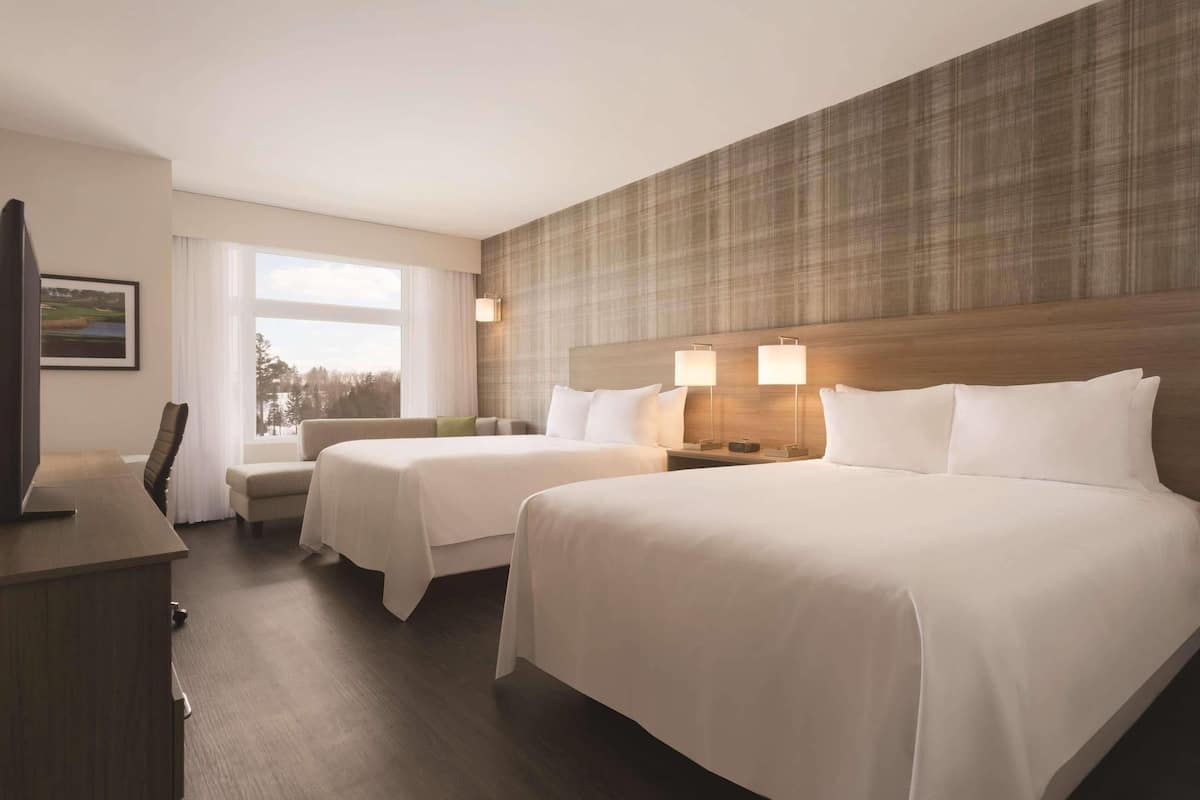 A hotel room with two beds, a desk, a chair, and a TV.