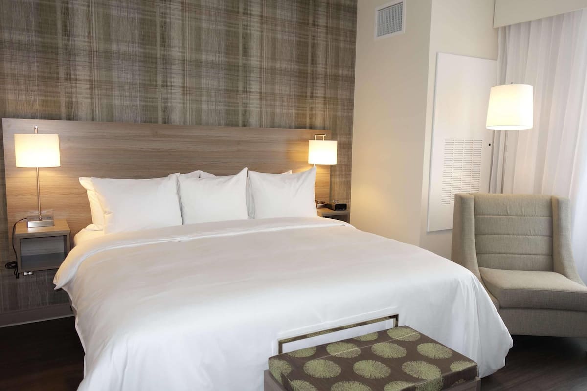 A hotel room with a large bed, two bedside lamps, a chair, and a small table.