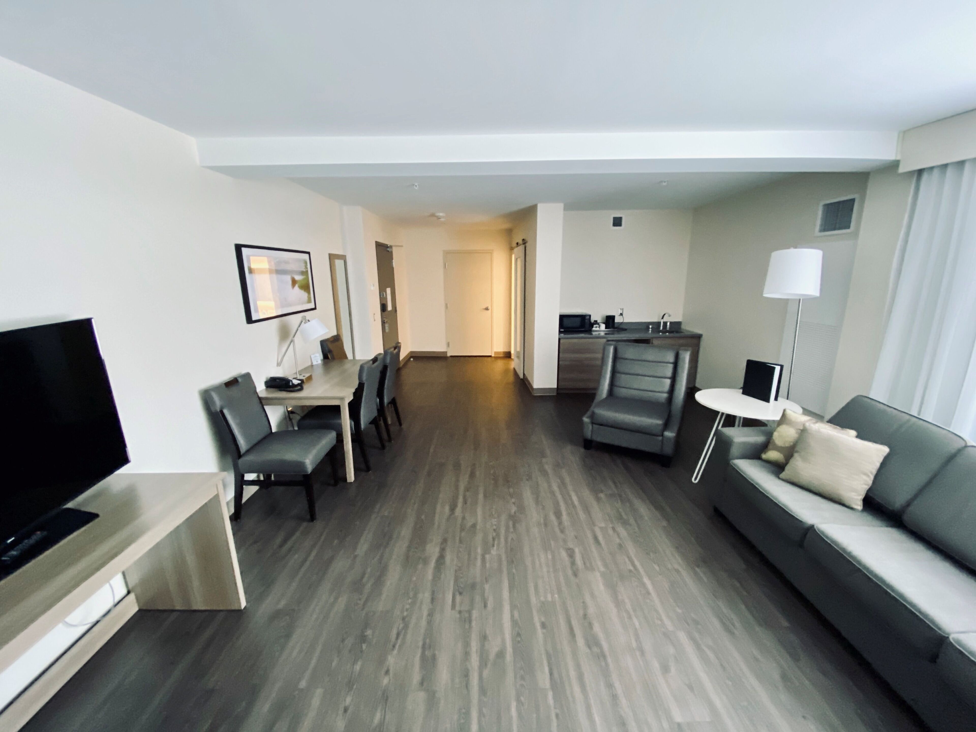 Une chambre d’hôtel moderne équipée d’un téléviseur à écran plat, d’un coin repas avec une table et des chaises, d’un canapé, d’un petit coin cuisine et d’un couloir menant à une autre chambre.