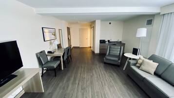 Une chambre d’hôtel moderne équipée d’un téléviseur à écran plat, d’un coin repas avec une table et des chaises, d’un canapé, d’un petit coin cuisine et d’un couloir menant à une autre chambre.