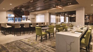 A modern restaurant with a bar area, green upholstered chairs, and a marble island. - Radisson Hotel Kingswood Hotel Fredericton, NB (Hanwell)