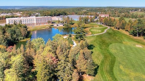 A golf course with a pond, surrounded by trees and a building with multiple windows. - Radisson Hotel Kingswood Hotel Fredericton, NB (Hanwell)