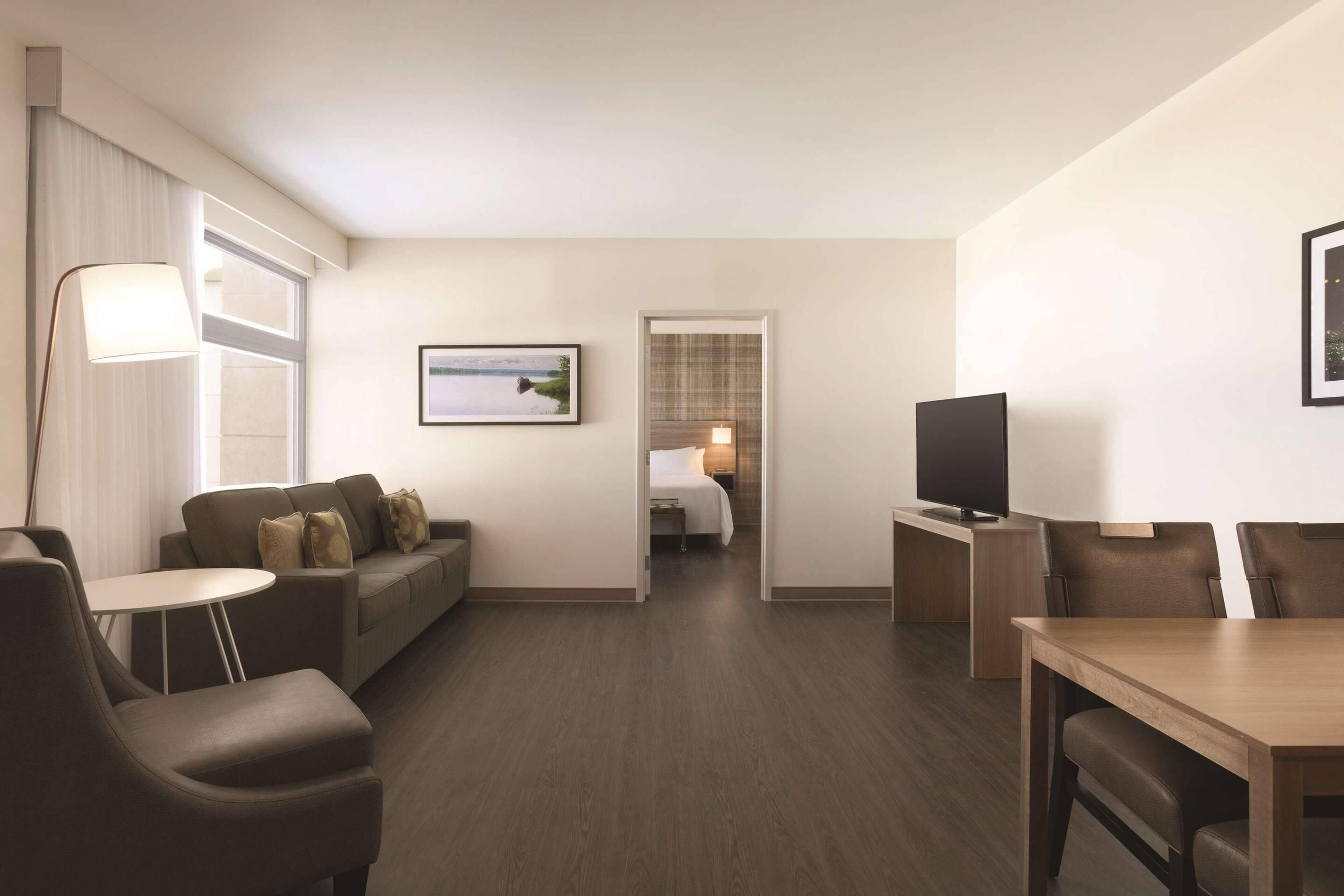 A hotel room with a sofa, a small round table, a TV, and a bed in the background.
