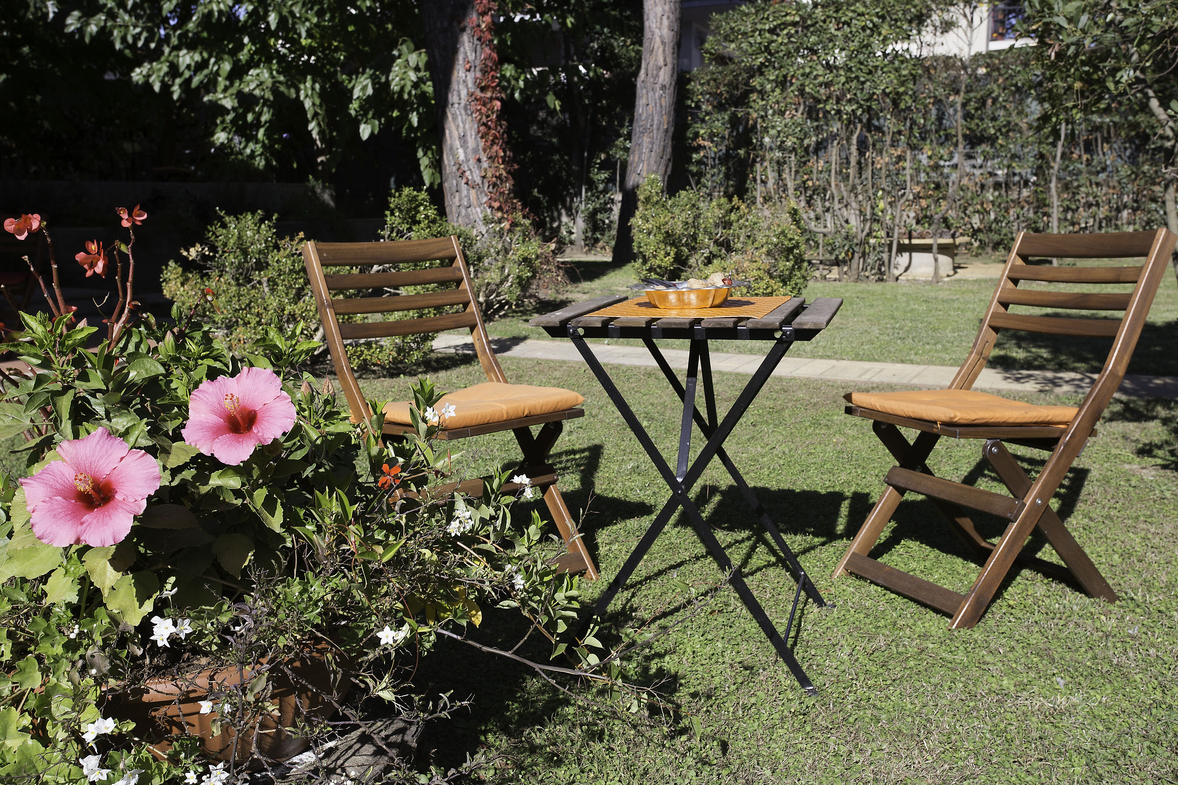 A garden with a wooden table and two chairs, surrounded by greenery and flowers.