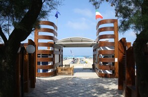 Une porte en bois, surmontée d’un toit incurvé, mène à une zone de plage où se trouve un banc et d’où l’on peut admirer la mer.