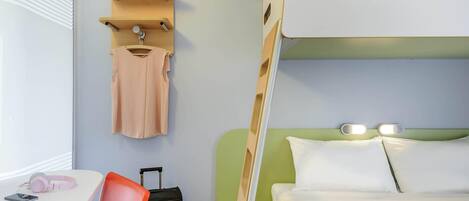 Une chambre d’hôtel avec un lit superposé, un bureau avec une chaise, une valise et un porte-manteau mural.