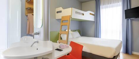 Una habitación de hotel con literas, un escritorio con silla, un lavamanos y una televisión.