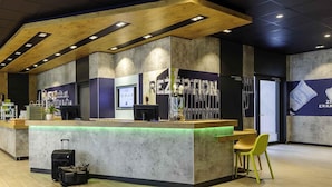 A reception area with a wooden counter, a computer, and a seating area with chairs. - Ibis Budget Bamberg (Bamberg)