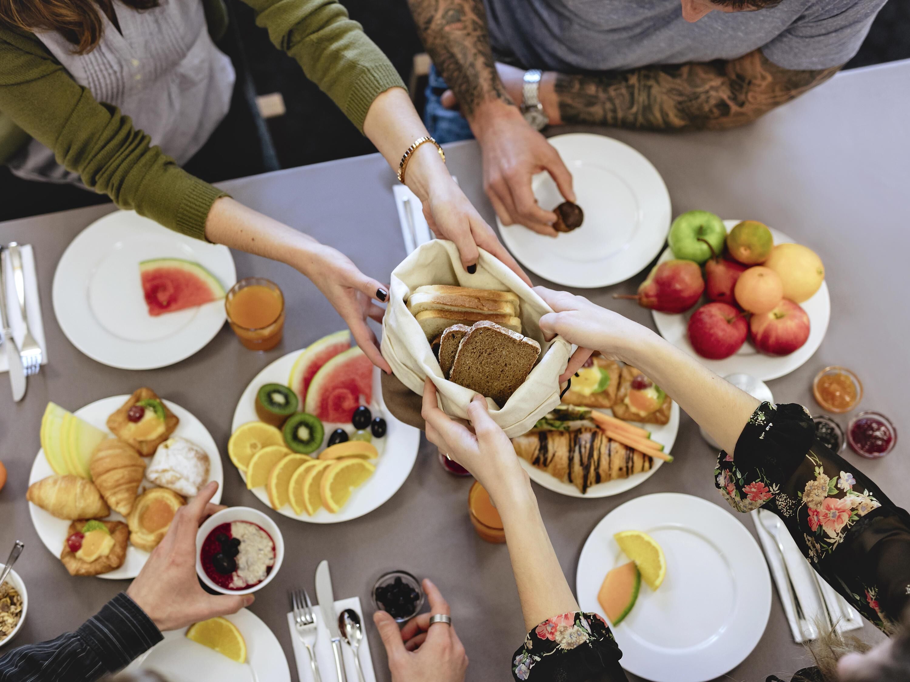 A group of people sharing a meal with various dishes including bread, fruits, and pastries.
