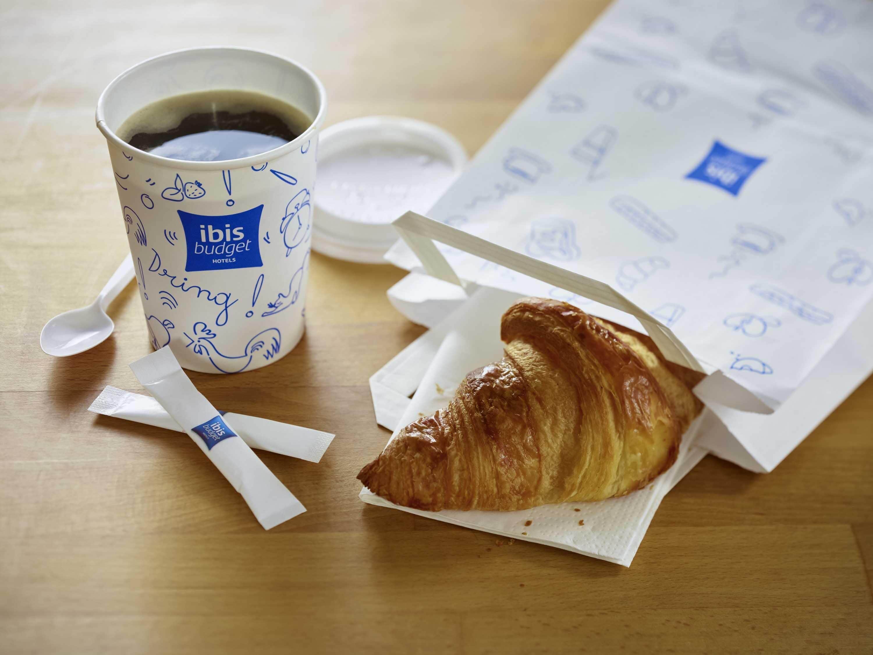 A cup of coffee, a croissant, and a napkin on a wooden table.