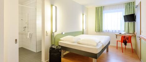 Ein Hotelzimmer mit Bett, Schreibtisch, Stuhl, Fernseher und einem Badezimmer mit Dusche und Toilette.