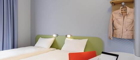 Habitación de hotel con dos camas, una mesita con un cuaderno y un bolígrafo, un teléfono inteligente y una chaqueta colgada.