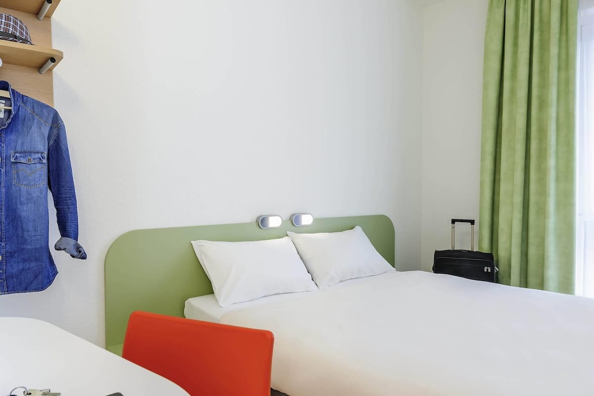 A hotel room with two beds, a desk with keys, a suitcase, and a denim jacket on a shelf.