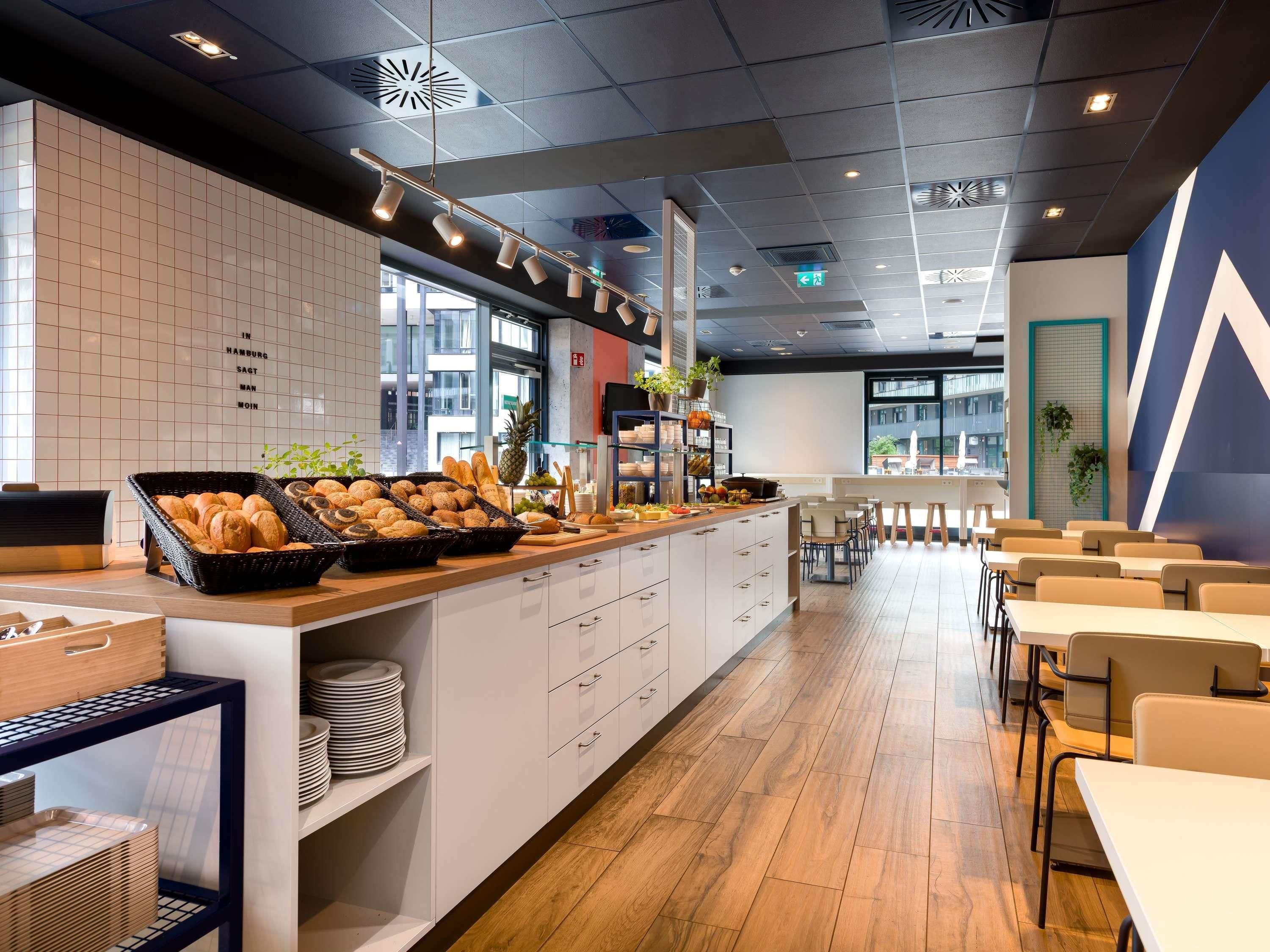 A modern cafe with a buffet counter, seating area, and a view of the cityscape.