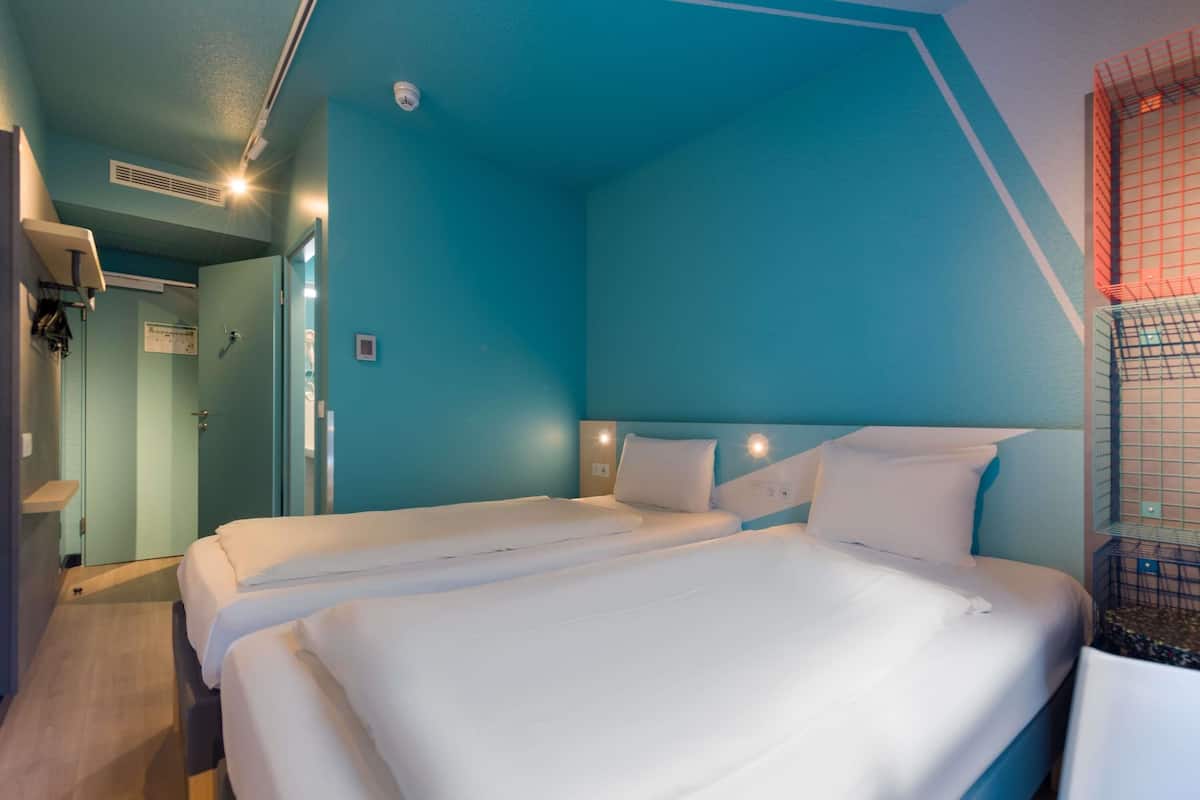 Een kamer met twee bedden, een plafondventilator, een lamp en een deur.