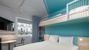 Een stapelbed met een televisie, bureau en raam met uitzicht op gebouwen.