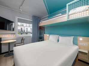 A bunk bed with a TV, a desk, and a window with a view of buildings. - Ibis Budget Hamburg City (Hamburg)