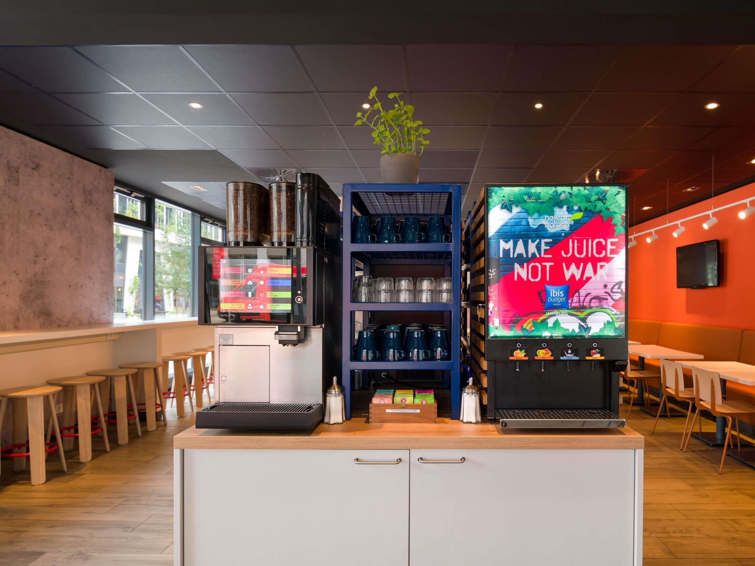 A modern juice bar with a coffee machine, a shelf with cups, and a large juice dispenser.