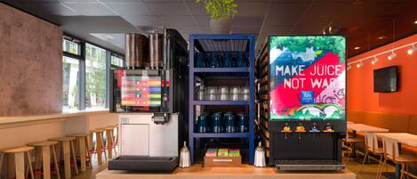 A modern juice bar with a coffee machine, a shelf with cups, and a large juice dispenser.