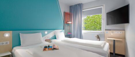 A hotel room with a large bed, a TV, a window with a view of greenery, and a bedside table.