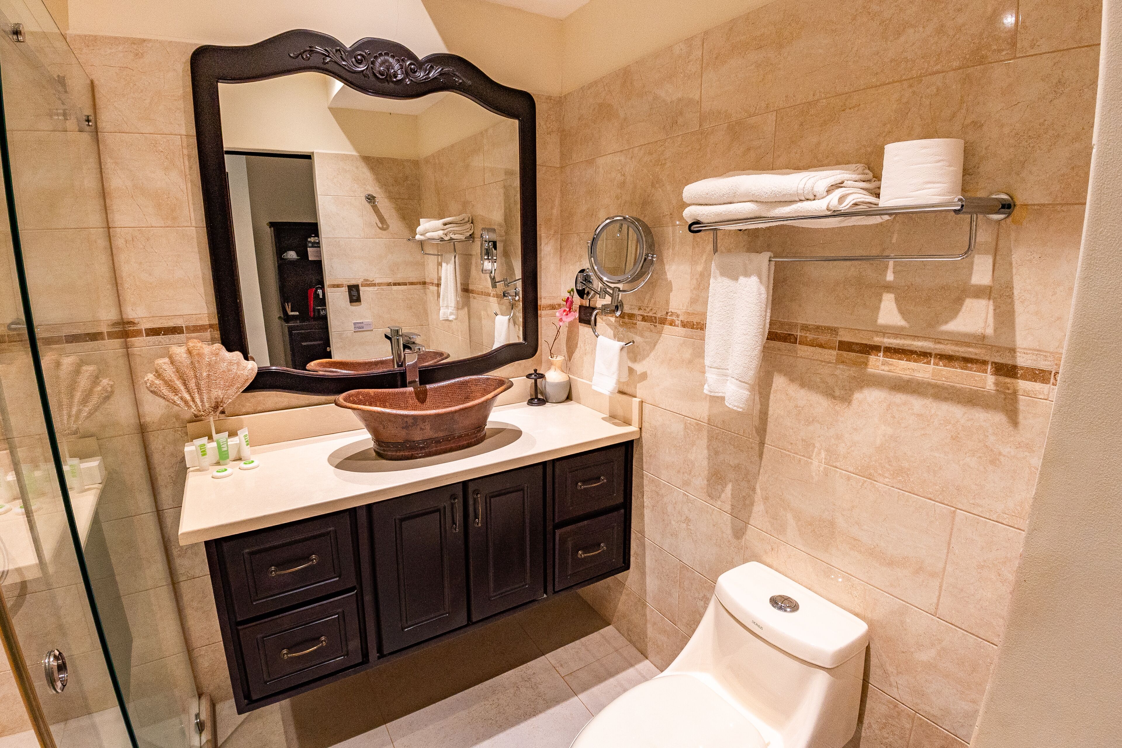 A bathroom with a large mirror, a sink with a decorative bowl, a toilet, and a towel rack with folded towels.