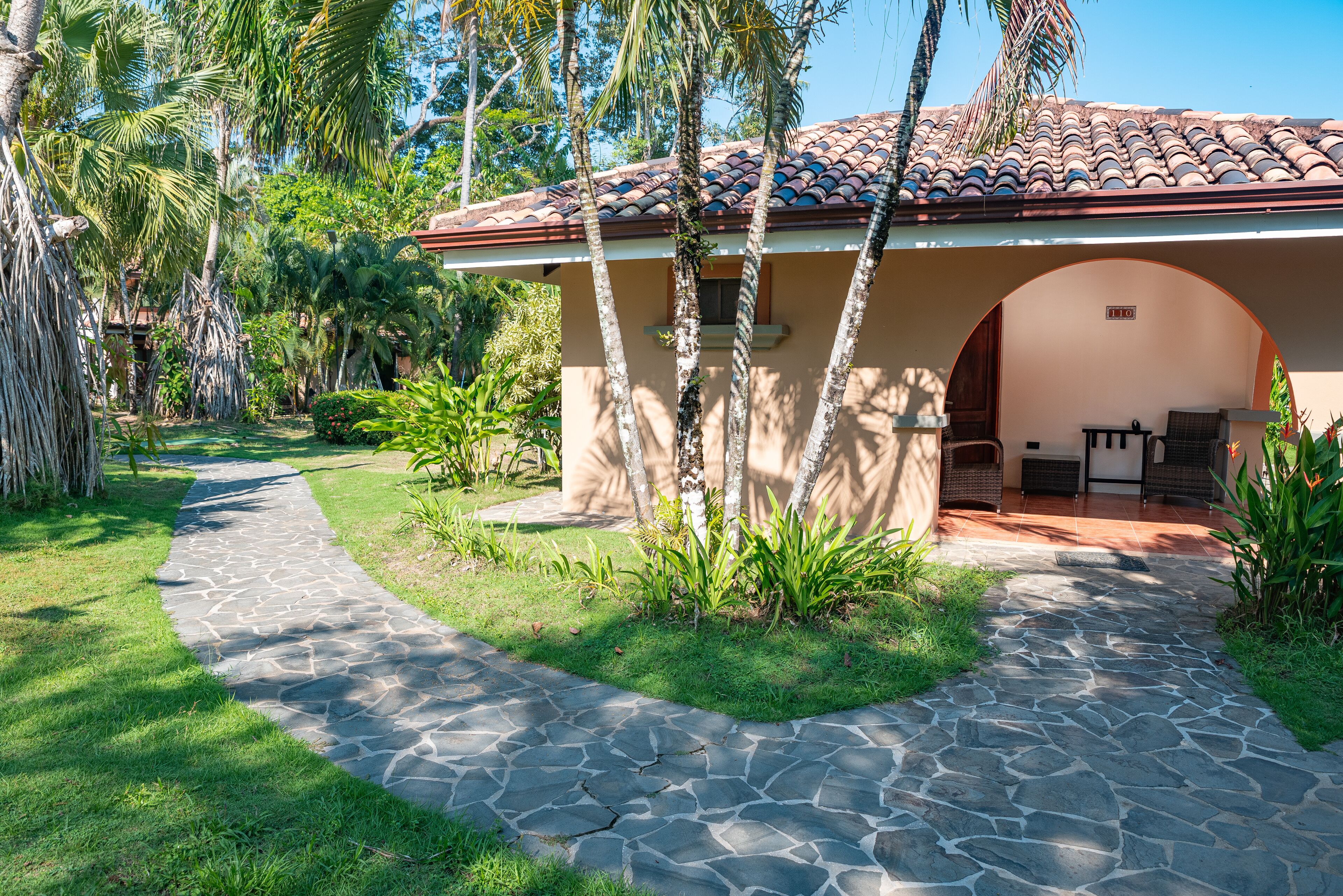 A stone pathway leading to a building with a tiled roof and an archway entrance.