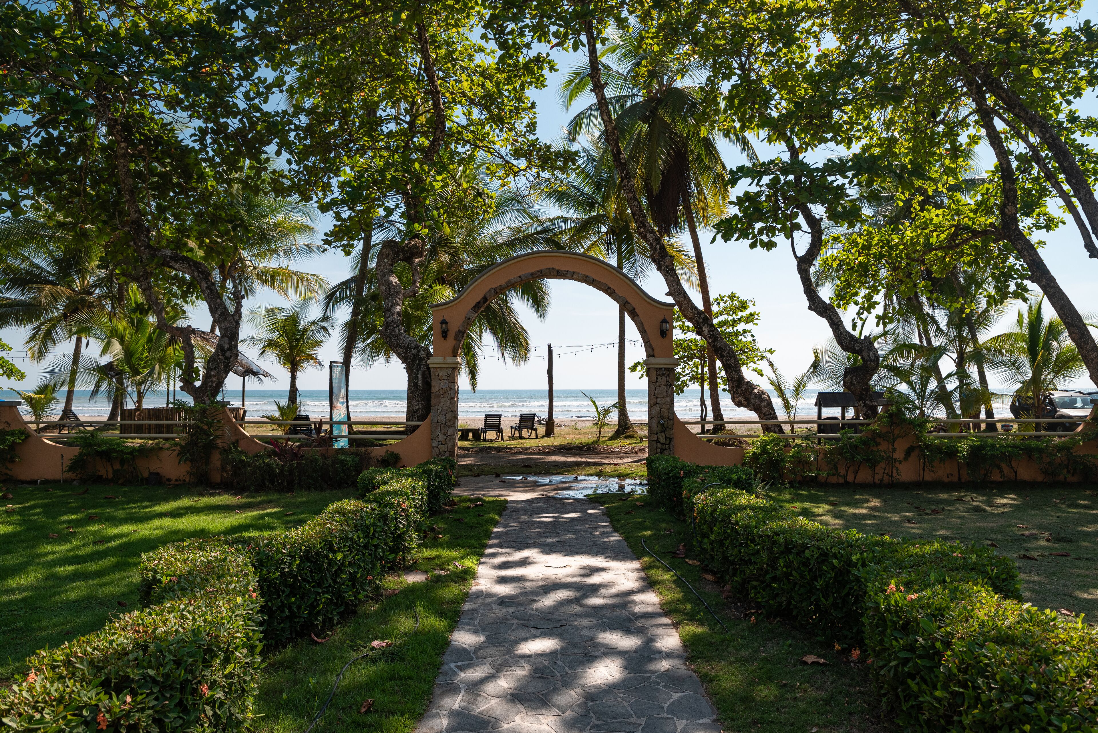 A pathway leading to a beach area with palm trees and a stone archway.