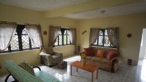 A living room with a sofa, a chair, a coffee table, and a window with curtains. - Rocky Top Retreat (Negril)
