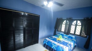 A bedroom with a bed, a wardrobe, a window with shutters, and a ceiling fan. - Rocky Top Retreat (Negril)