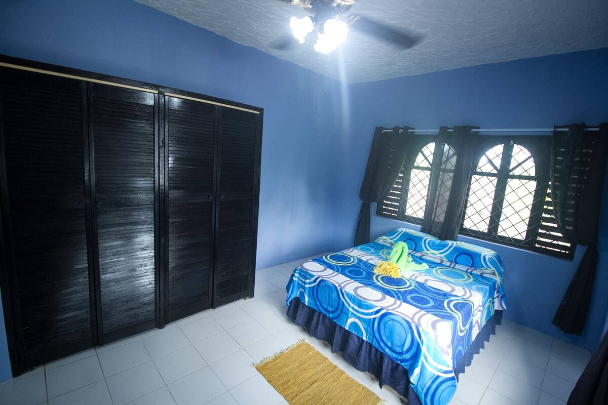 A bedroom with a bed, a wardrobe, a window with shutters, and a ceiling fan.