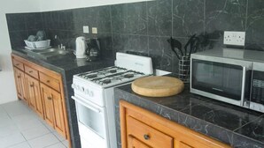 A kitchen with a stove, microwave, and wooden cabinets. - Rocky Top Retreat (Negril)