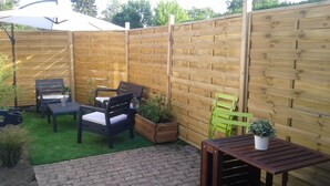 Une terrasse avec des meubles en bois, un chemin en briques et une clôture en bois.