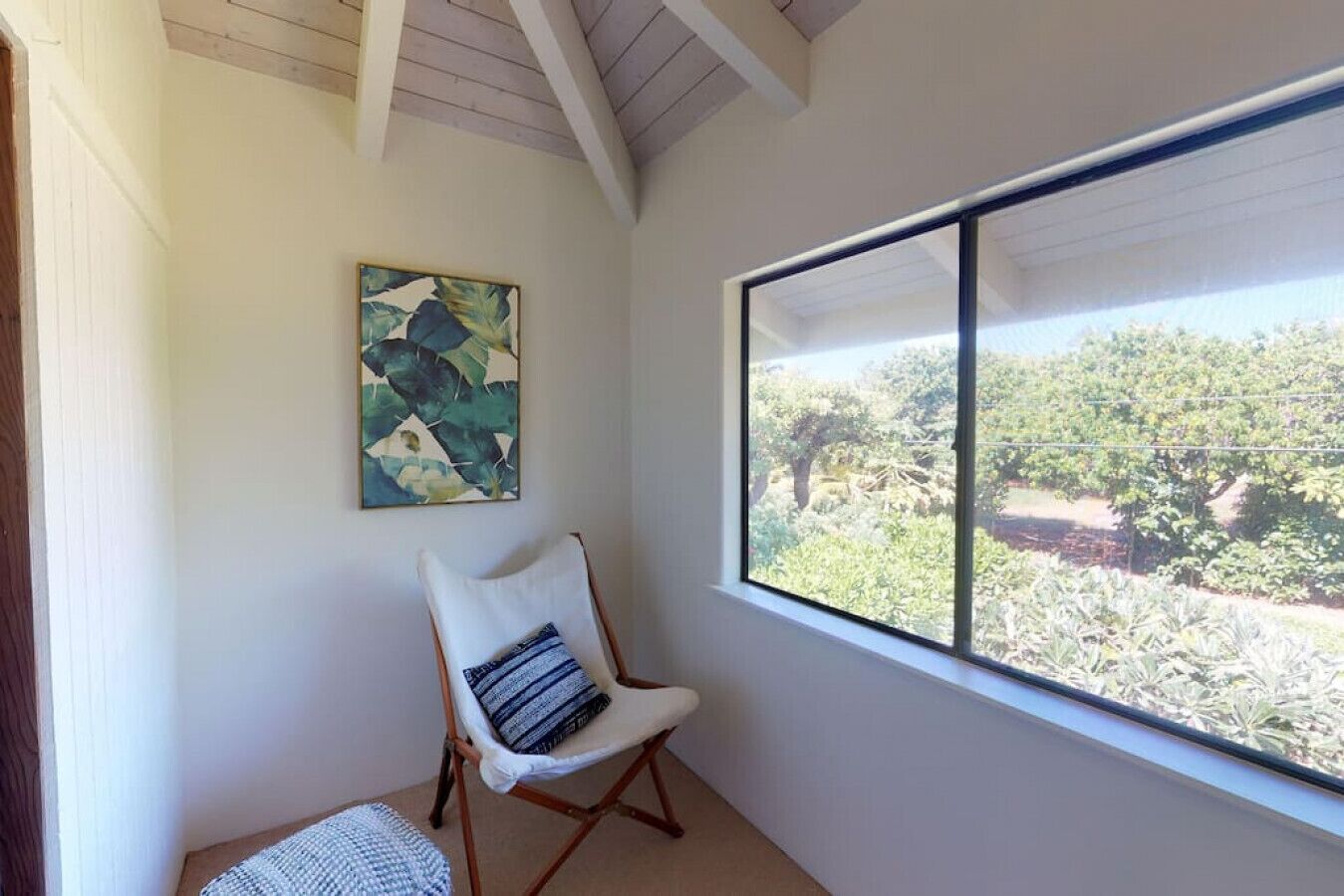 Una habitación con un ventanal grande, una silla blanca con cojín y un cuadro en la pared.