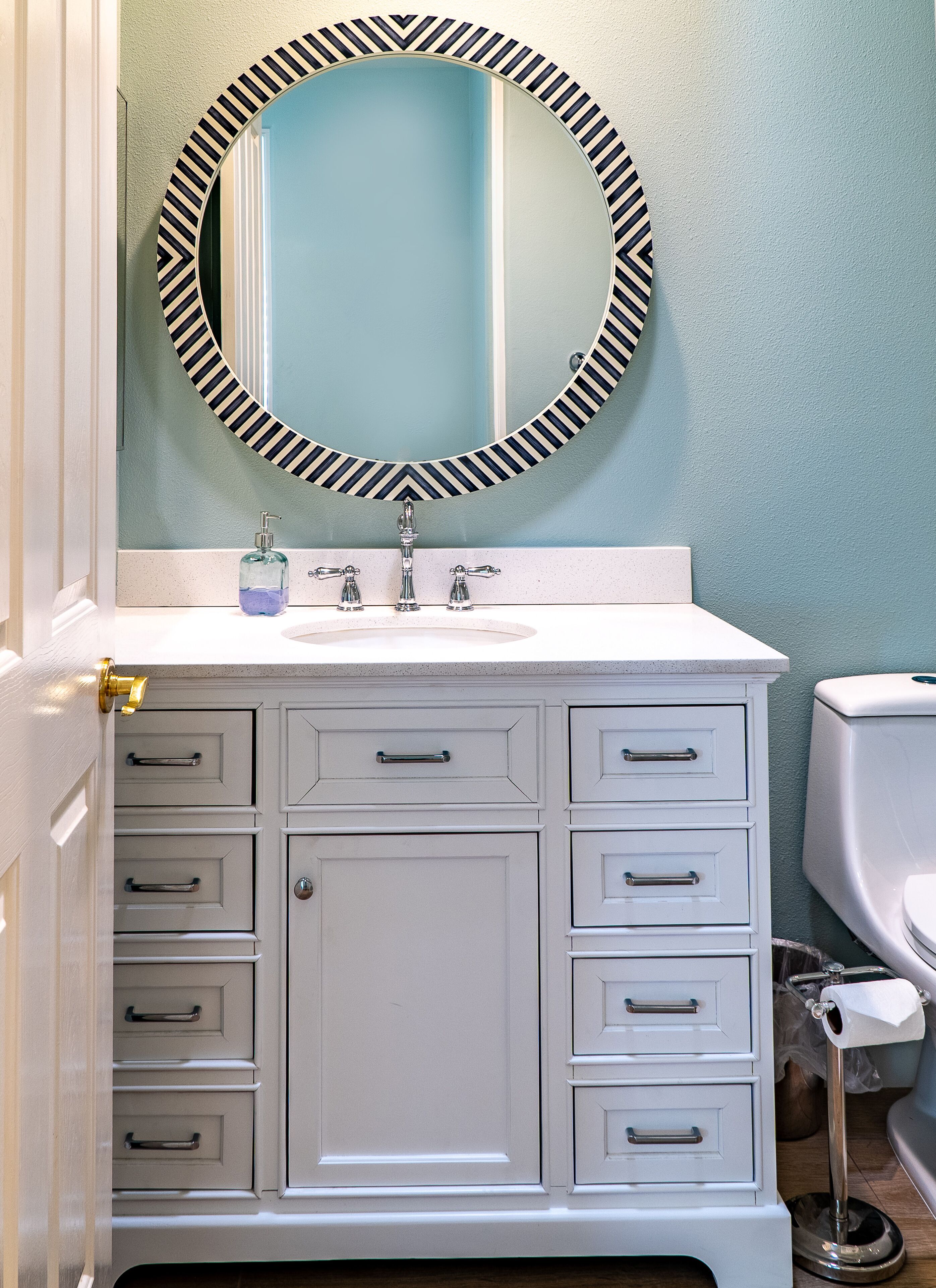 Een badkamer met een witte wastafel, een ronde spiegel met een zwart-wit gestreept frame, en een toilet.