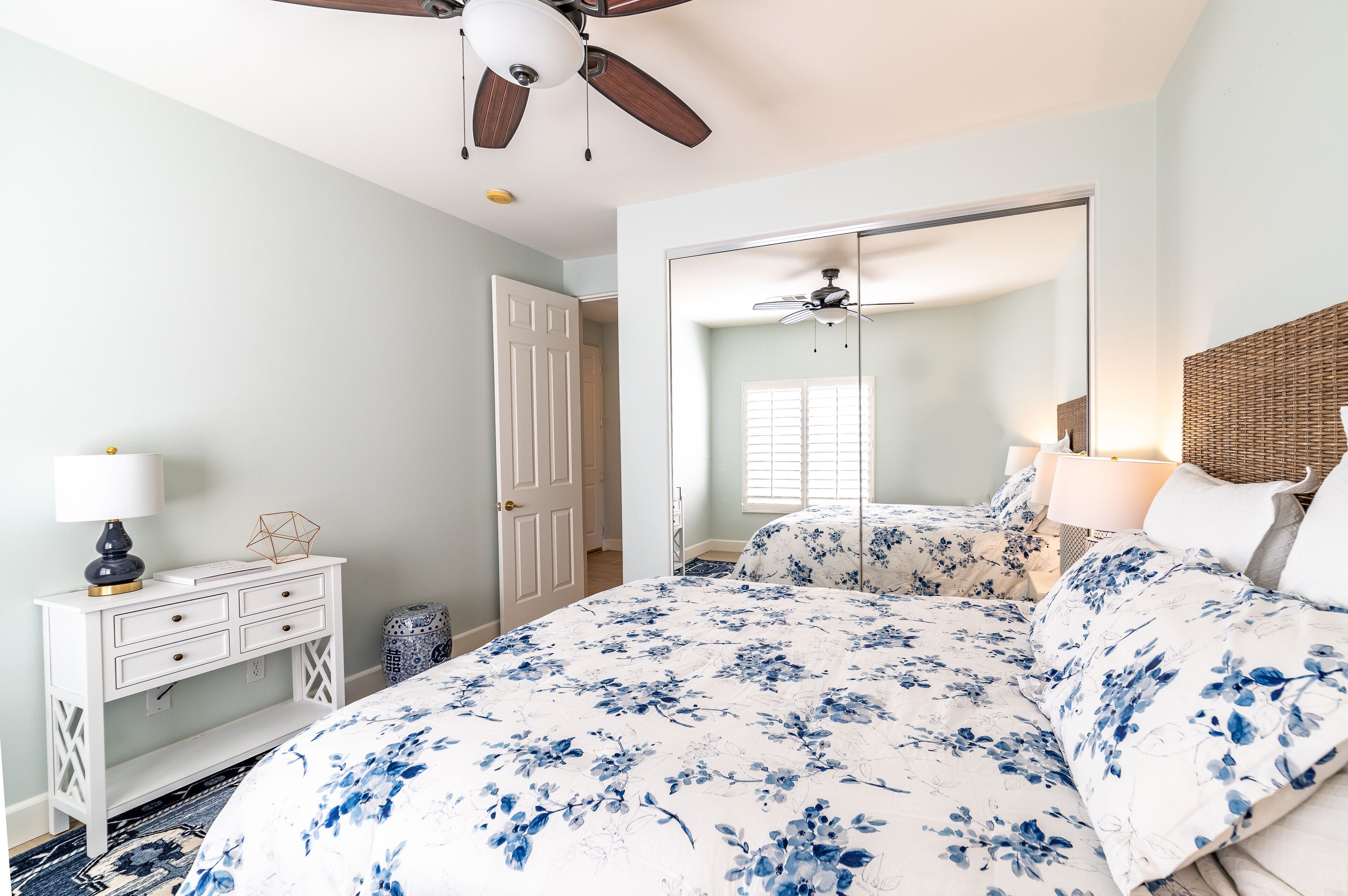 A bedroom with a bed, a dresser, a ceiling fan, and a mirror.