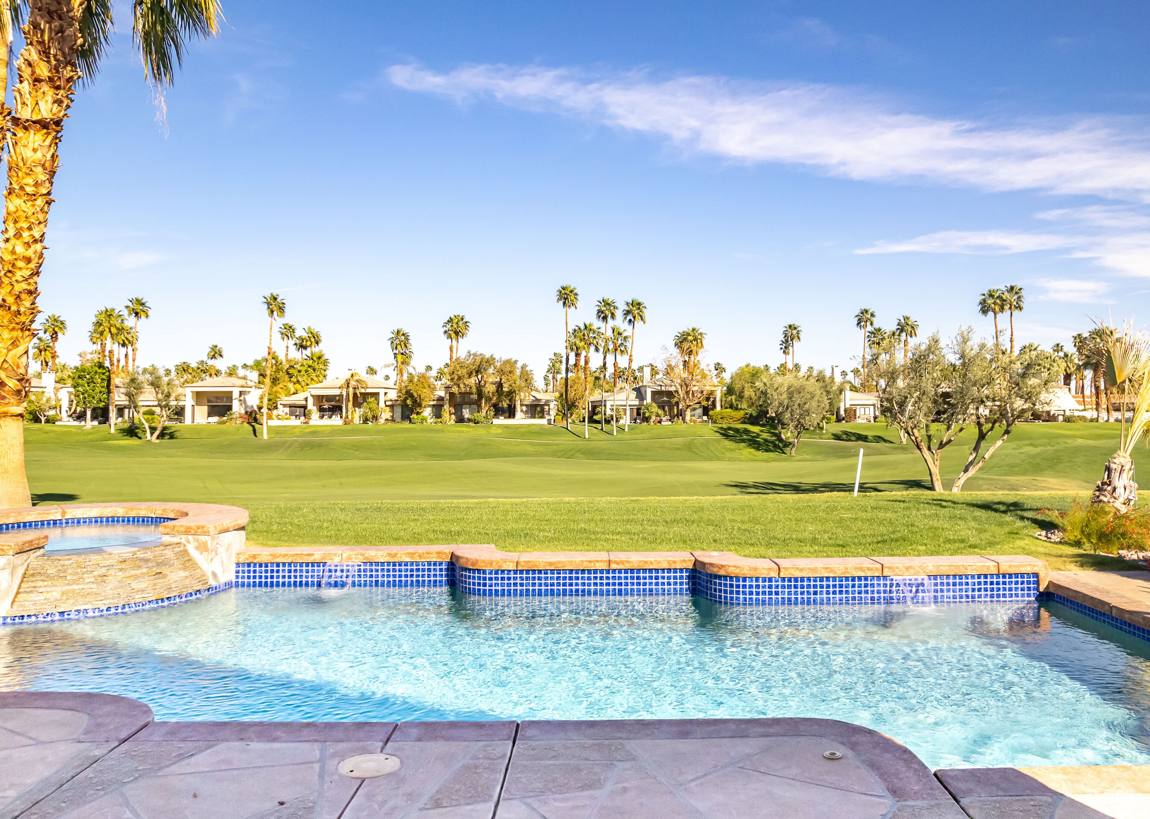 A swimming pool with a view of a golf course and palm trees.