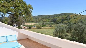 A balcony with a blue table and chairs, overlooking a green landscape with hills.