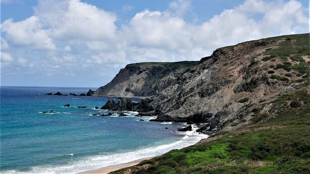 A coastal landscape with a beach, rocky cliffs, and a clear sky.