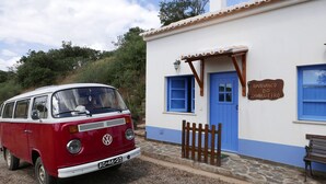 A red and white van parked in front of a building with a blue door and windows, a wooden fence, and a bench.