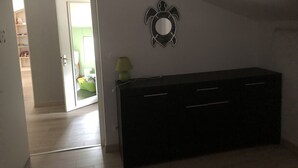 Une pièce avec une commode de couleur sombre, un miroir fixé au mur et une porte donnant sur une autre pièce.
